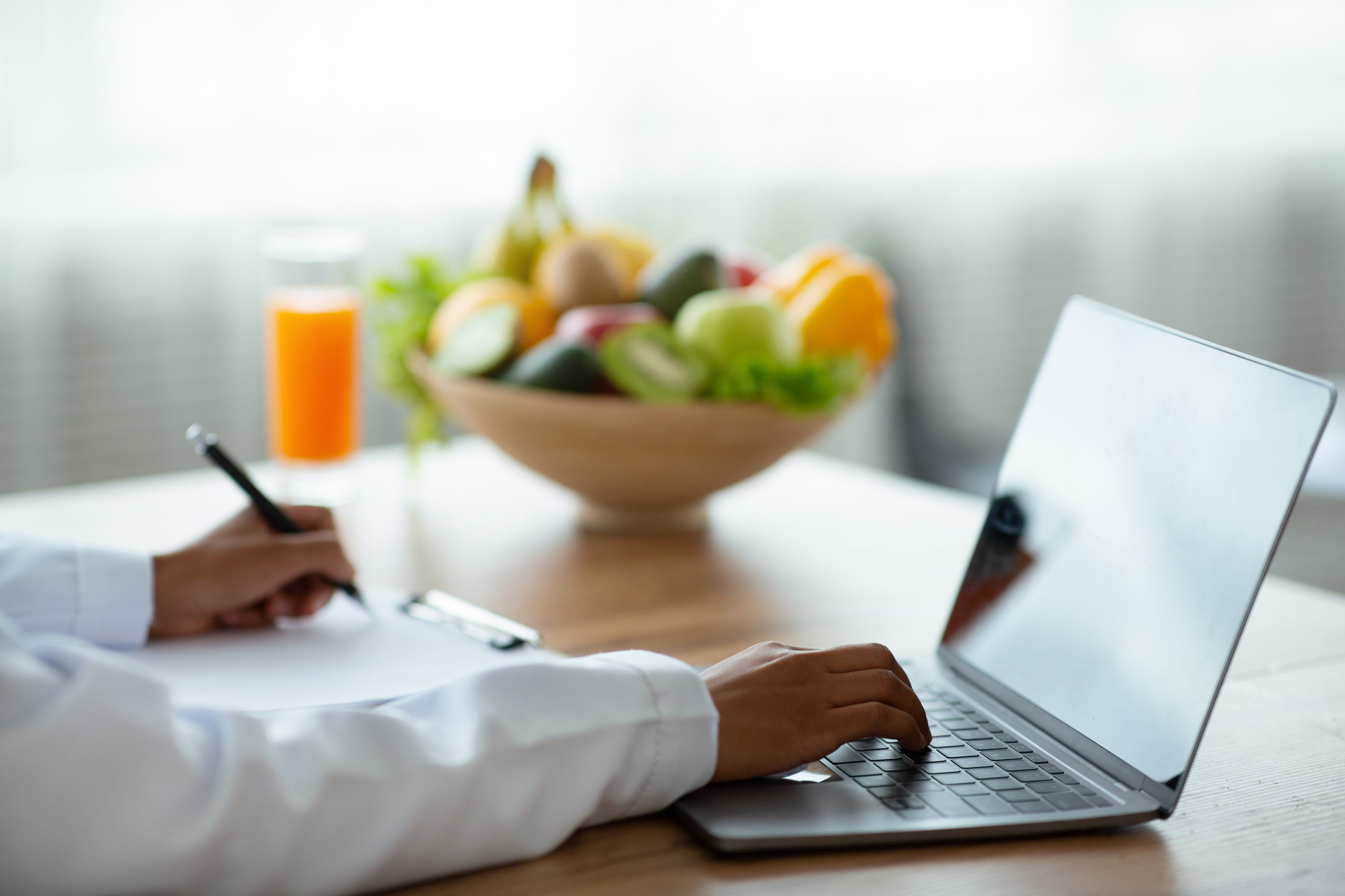Healthy nutrition specialist giving online consultation, mockup for design on laptop screen. Cropped view of black female dietologist typing on pc keyboard and taking notes at office